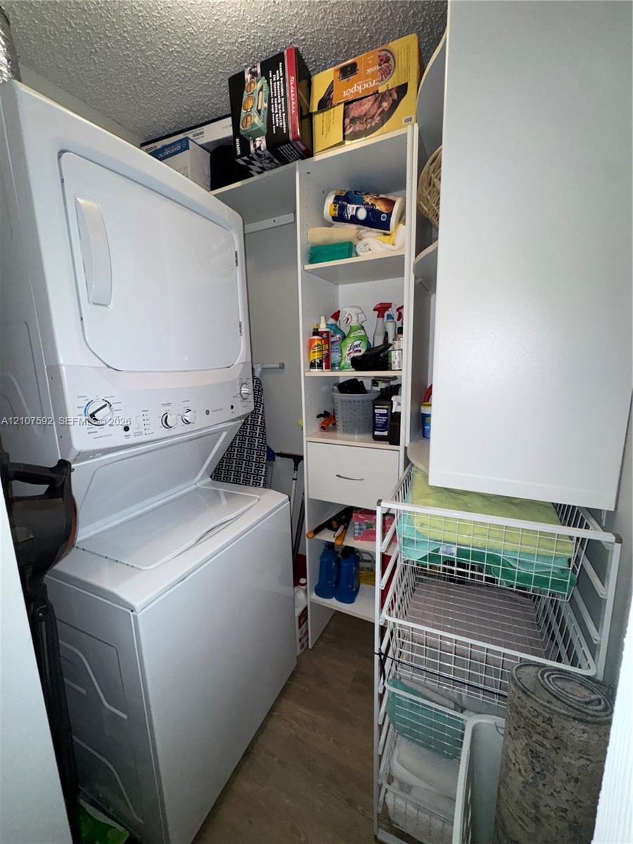 Laundry closet featuring a stackable washer and dryer, white built-in shelving unit, and wood-finish flooring