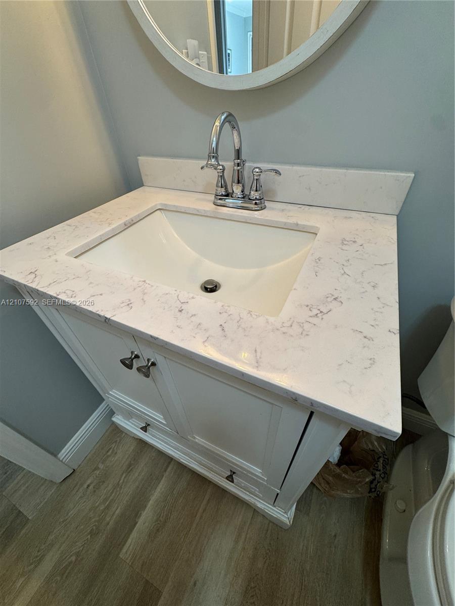 White vanity cabinet with integrated storage, engineered stone countertop, undermount sink, dual-handle chrome faucet, and circular wall-mounted mirror
