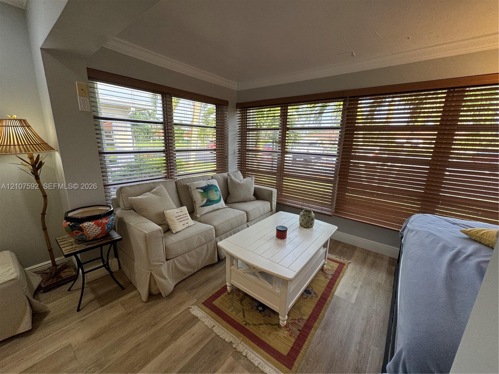 Expansive corner window configuration with horizontal wood-finish blinds and neutral wall finishes, complemented by durable wood-finish flooring and crown molding