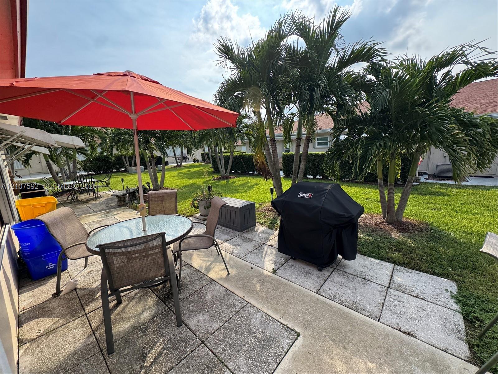 Rear patio featuring concrete pavers, landscaped lawn, and mature palm trees