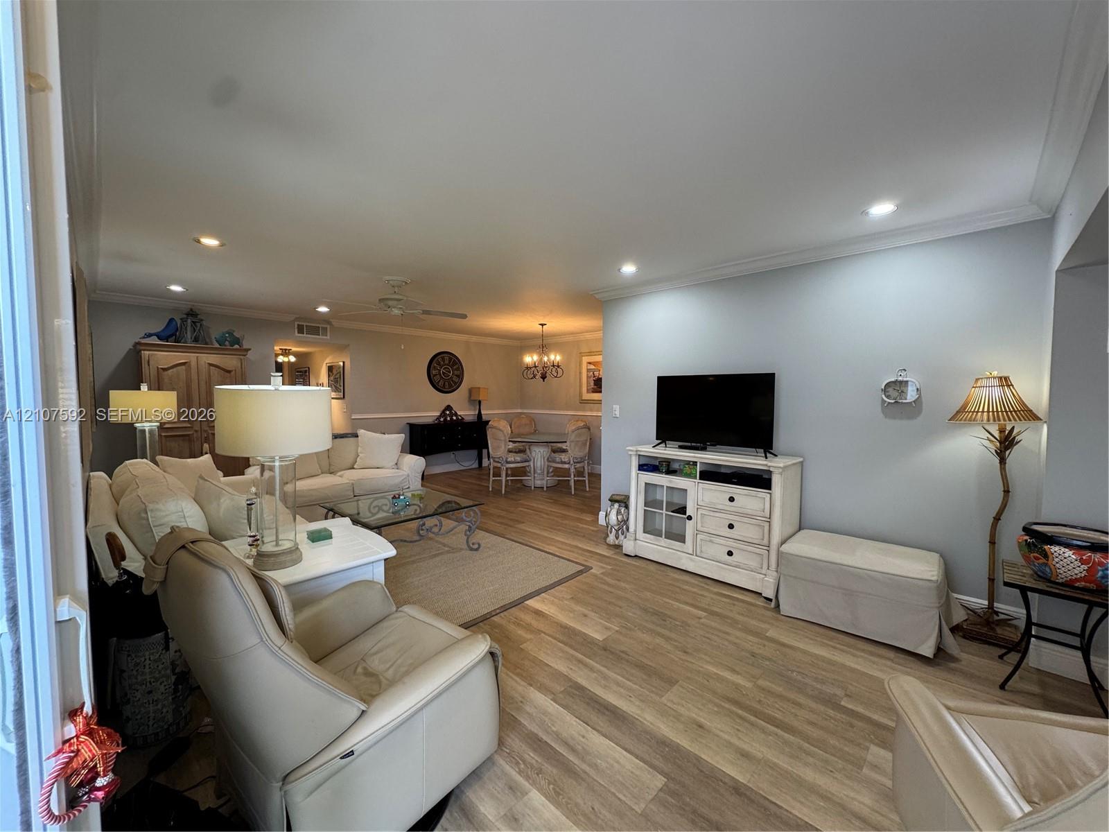 Open-concept living space featuring wood-finish flooring, recessed lighting, and crown molding Open-concept living space featuring wood-finish flooring, recessed lighting, and crown molding