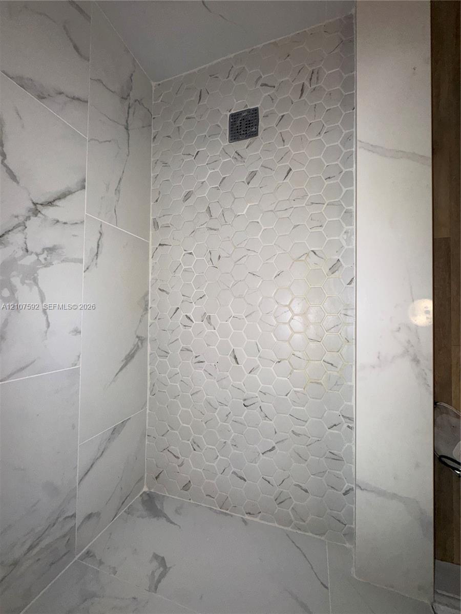 Shower enclosure featuring large-format rectified wall tile, decorative hexagon-patterned accent tile, and integrated drain