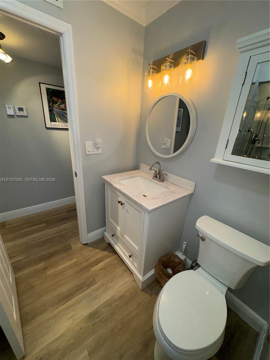 White vanity with a stone countertop, circular wall mirror, wood-finish flooring, three-light fixture, and wall-mounted medicine cabinet