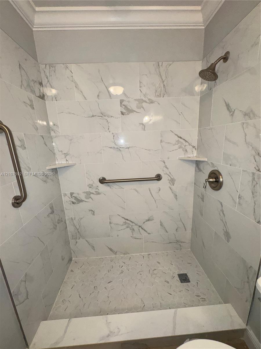 Walk-in shower featuring large-format stone-patterned wall tile, recessed corner shelving, a textured pebble floor, and brushed-finish plumbing fixtures