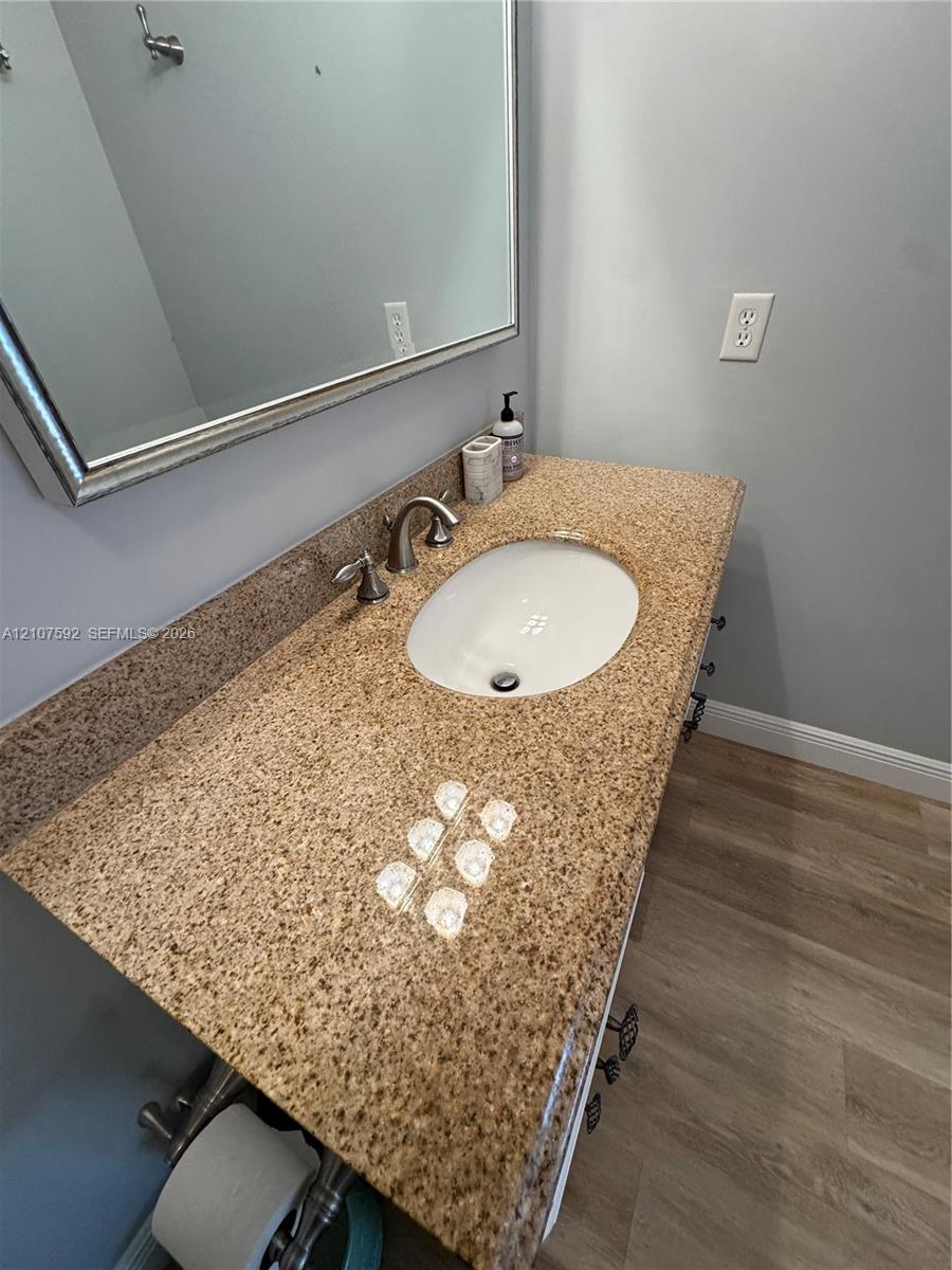 Bathroom vanity featuring a stone-composite countertop, undermount sink, brushed-metal faucet, wall-mounted mirror, and wood-finish flooring