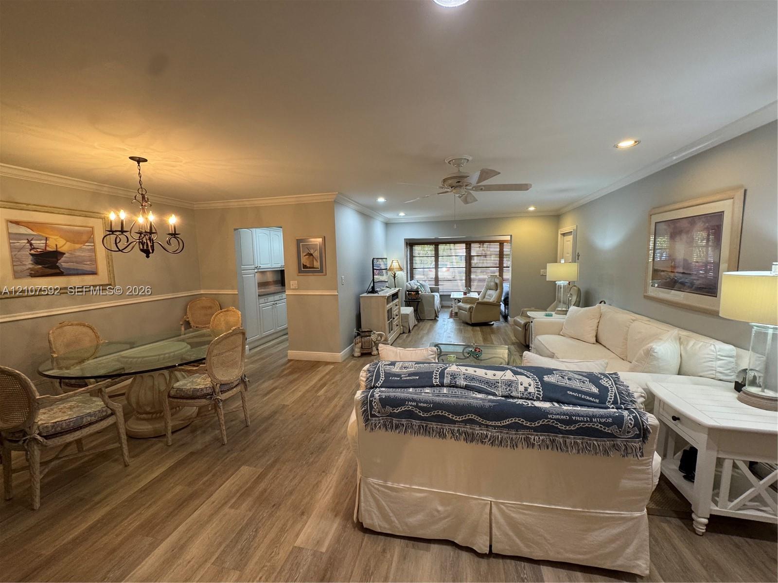Open-concept interior featuring wood-finish flooring, crown molding, chair rail trim, recessed lighting, and a multi-arm chandelier Open-concept interior featuring wood-finish flooring, crown molding, chair rail trim, recessed lighting, and a multi-arm chandelier