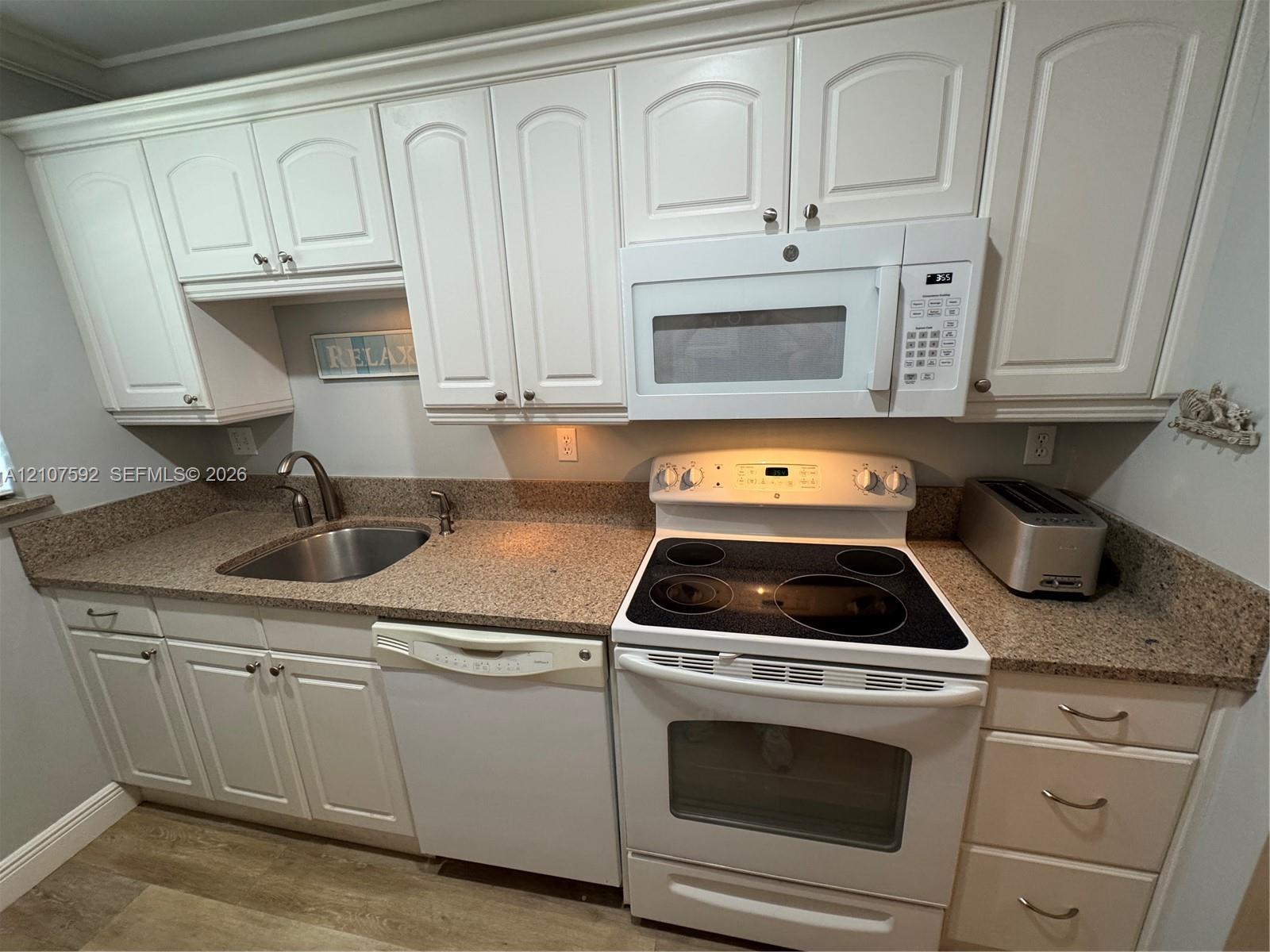 Kitchen featuring white cabinetry, stone-finish countertops, stainless steel sink with high-arc faucet, and white appliances including an electric range, over-the-range microwave, and dishwasher