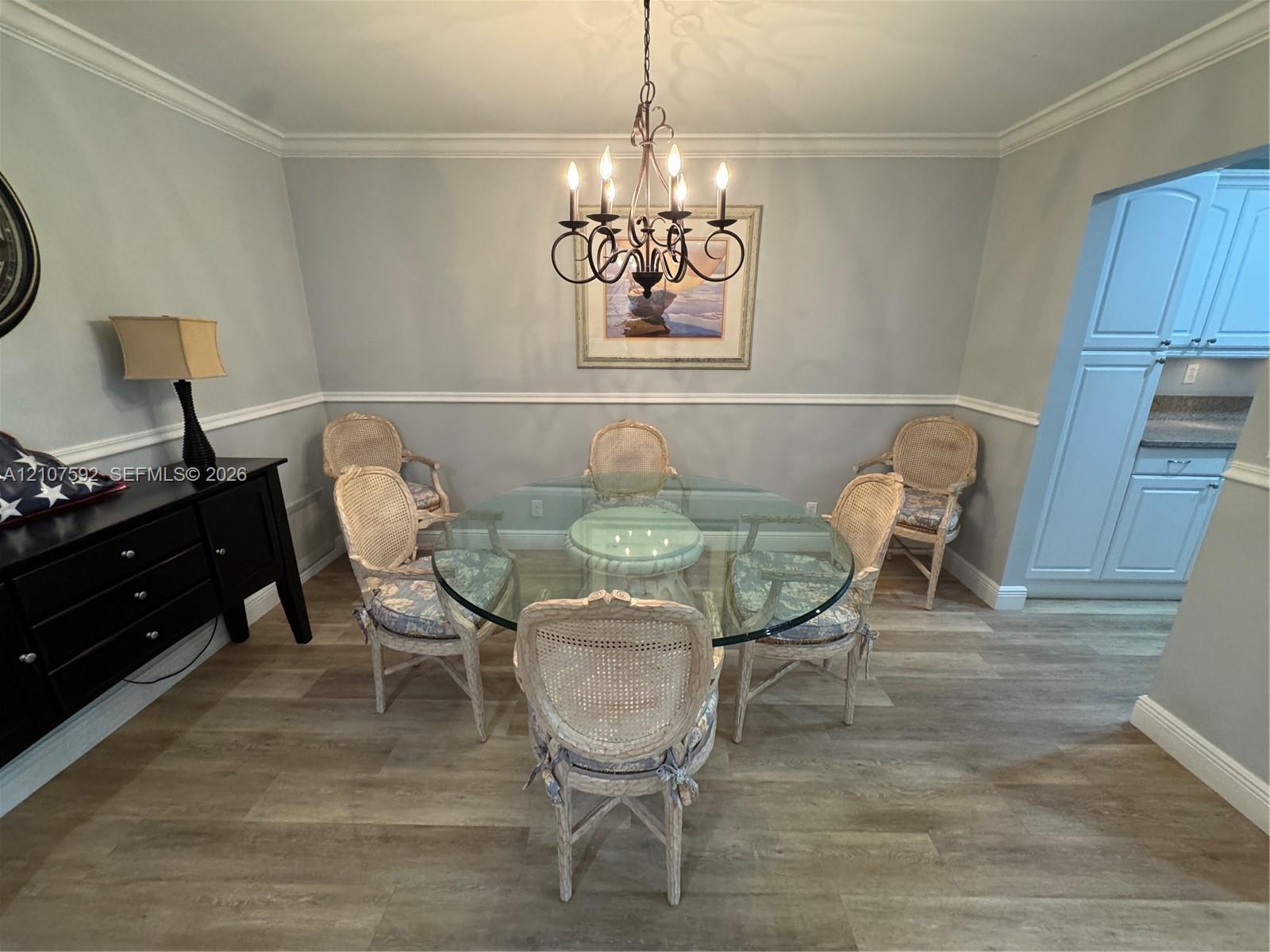 Dining area featuring wood-finish flooring, chair rail molding, crown molding, and a multi-arm candle-style chandelier Dining area featuring wood-finish flooring, chair rail molding, crown molding, and a multi-arm candle-style chandelier