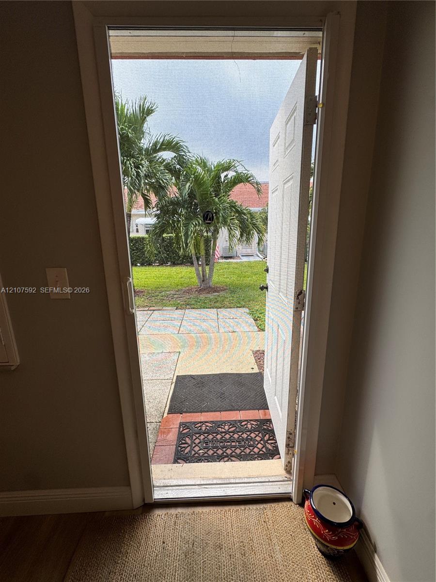 Paneled exterior door with integrated screen, concrete paver patio, and lawn area featuring mature palm trees