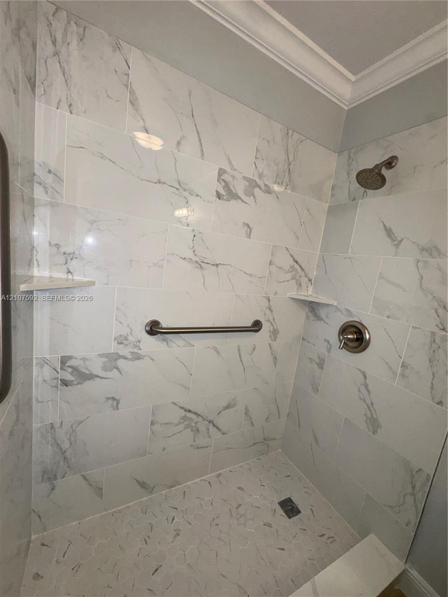 Shower enclosure featuring large-format wall tile with a neutral veined pattern, built-in corner shelving, stone-texture floor tiling, and a metallic finish shower head with matching control handle
