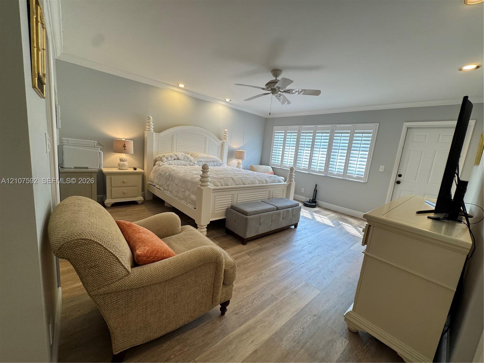 Bedroom featuring wood-finish flooring, plantation shutters, crown molding, and a ceiling fan with integrated lighting