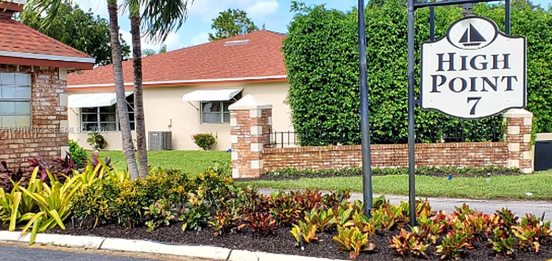 Stucco exterior featuring red shingled roofing, decorative brick pillars, metal window awnings, and landscaped garden beds