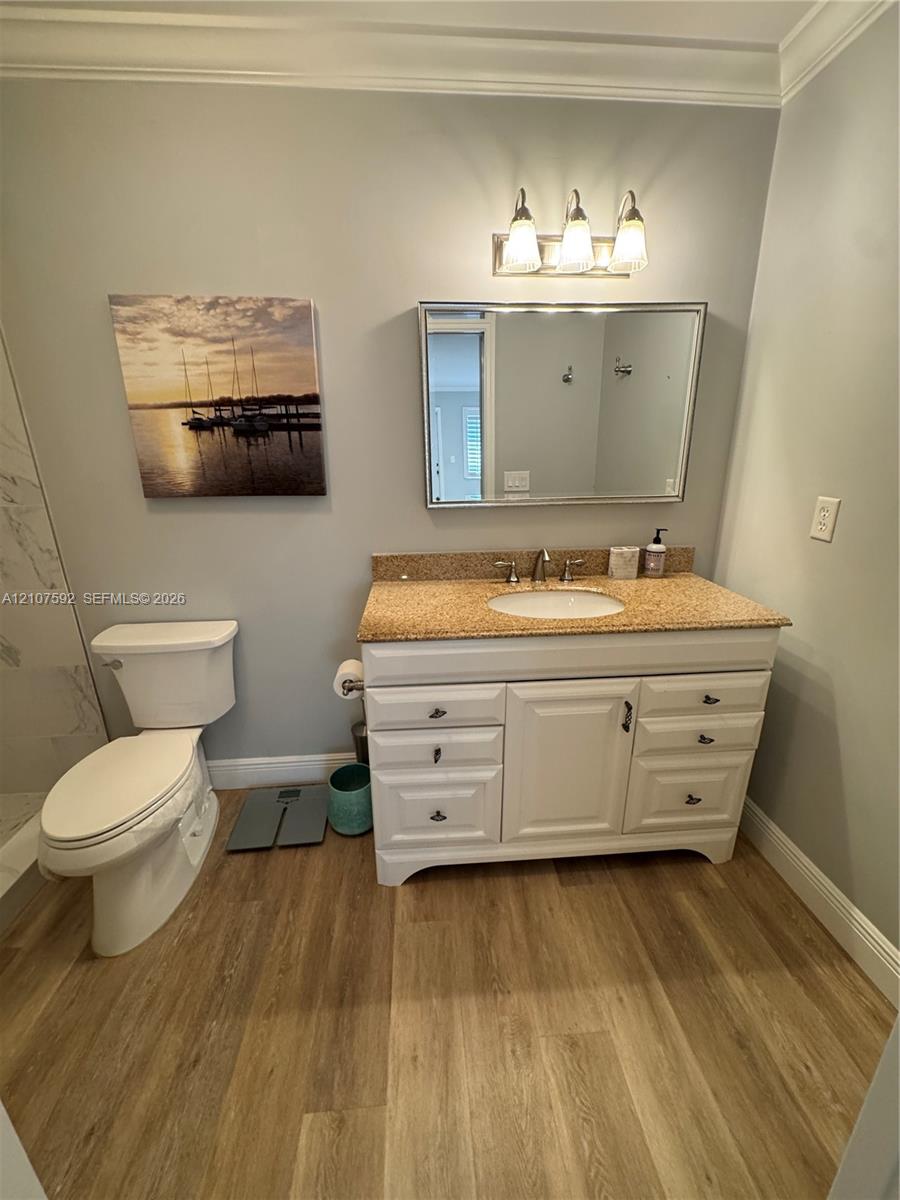 Vanity featuring a stone-composite countertop, undermount sink, and white shaker-style cabinetry, complemented by a tri-light fixture, framed wall mirror, and wood-finish flooring