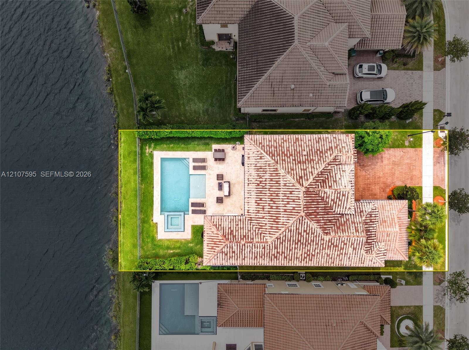 Waterfront property featuring a tiled roof, an inground swimming pool with a spa, stone-paver hardscaping, and a brick-paved driveway