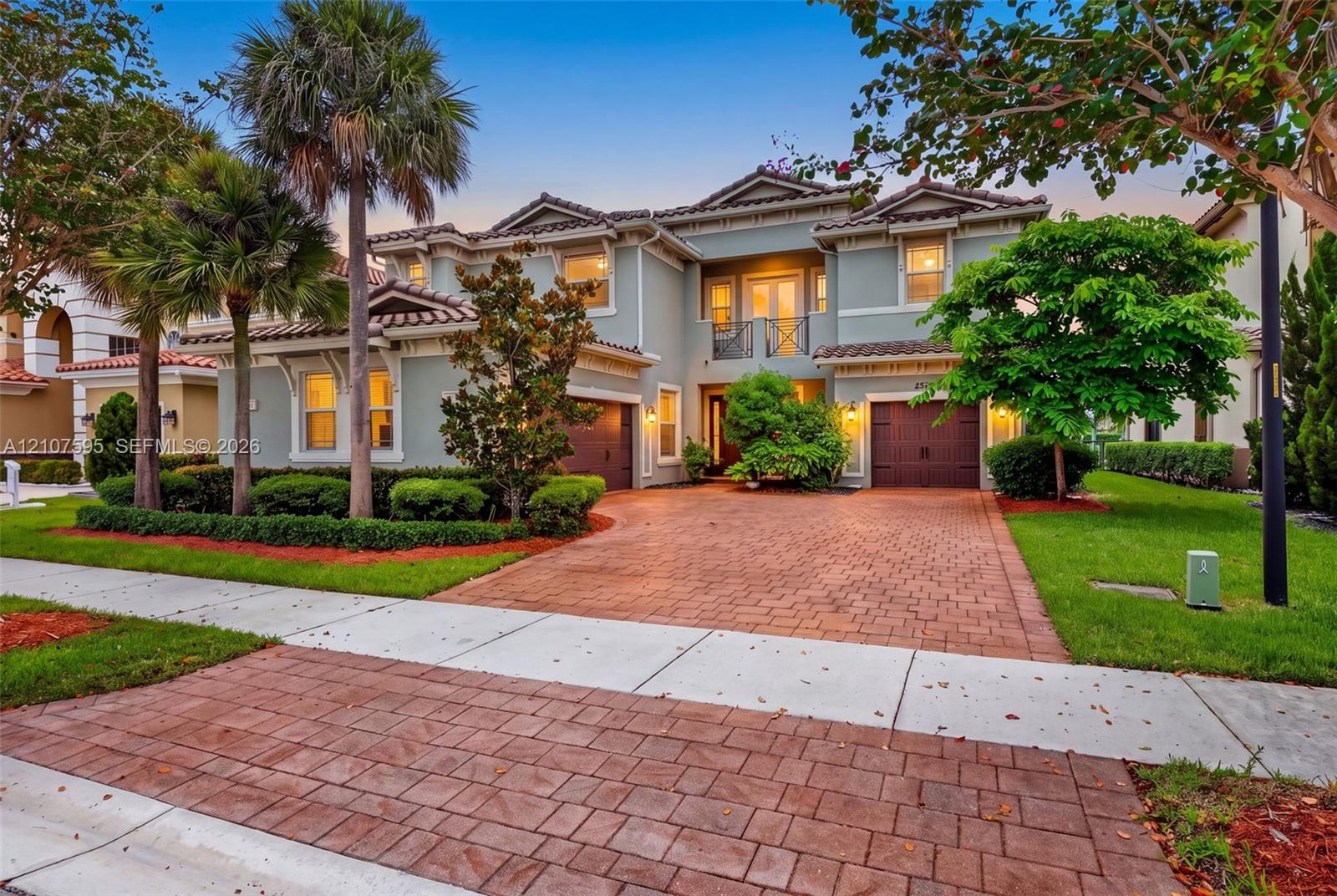 Two-story residence featuring a tile roof, stucco exterior, paver driveway, attached two-car garage, and second-story balcony with decorative metal railing