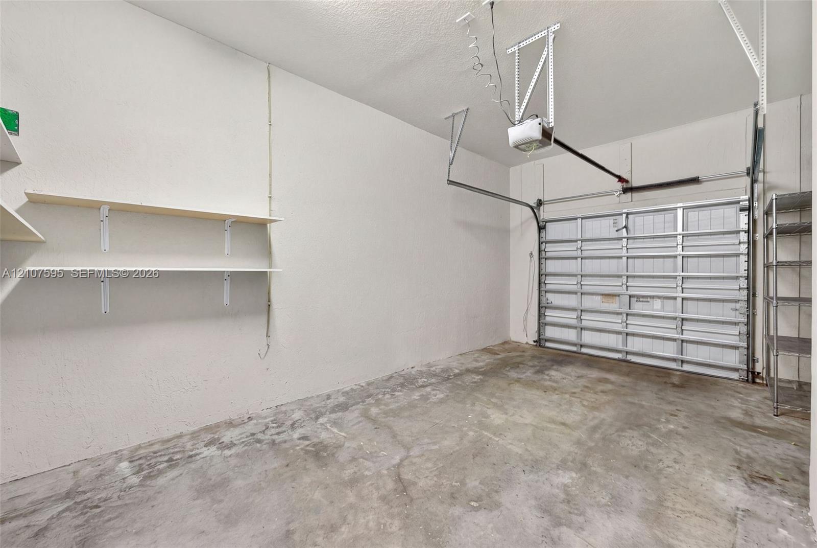 Attached garage featuring concrete flooring, a paneled overhead door, an automated ceiling-mounted door opener, and fixed wall-mounted shelving