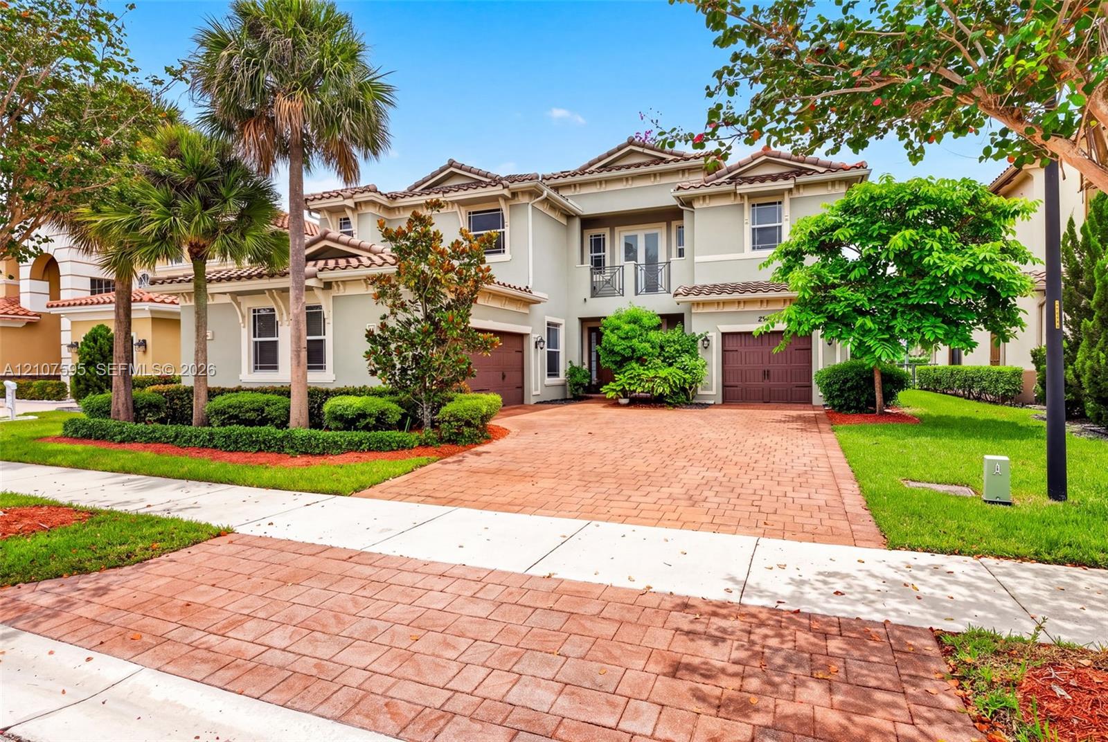 Two-story residence featuring a tile roof, stucco exterior, paver driveway, two-car garage, and a second-story iron railed balcony