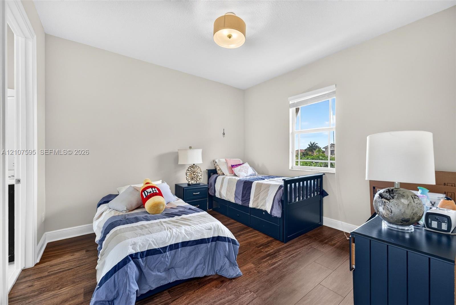 Neutral-toned walls, wood-finish flooring, a single-hung window with a roller shade, and a drum-style ceiling light fixture
