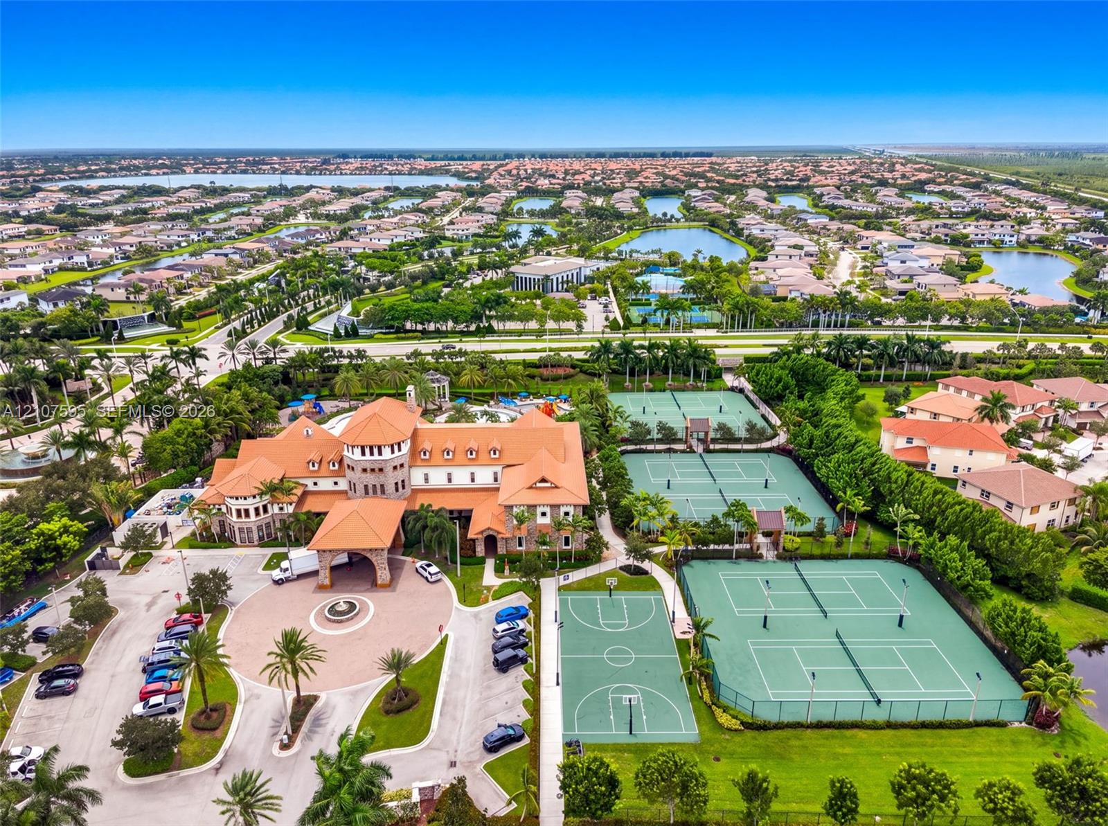 Mediterranean-style estate featuring a multi-story clubhouse, circular motor court with central fountain, multiple tennis courts, and a basketball court