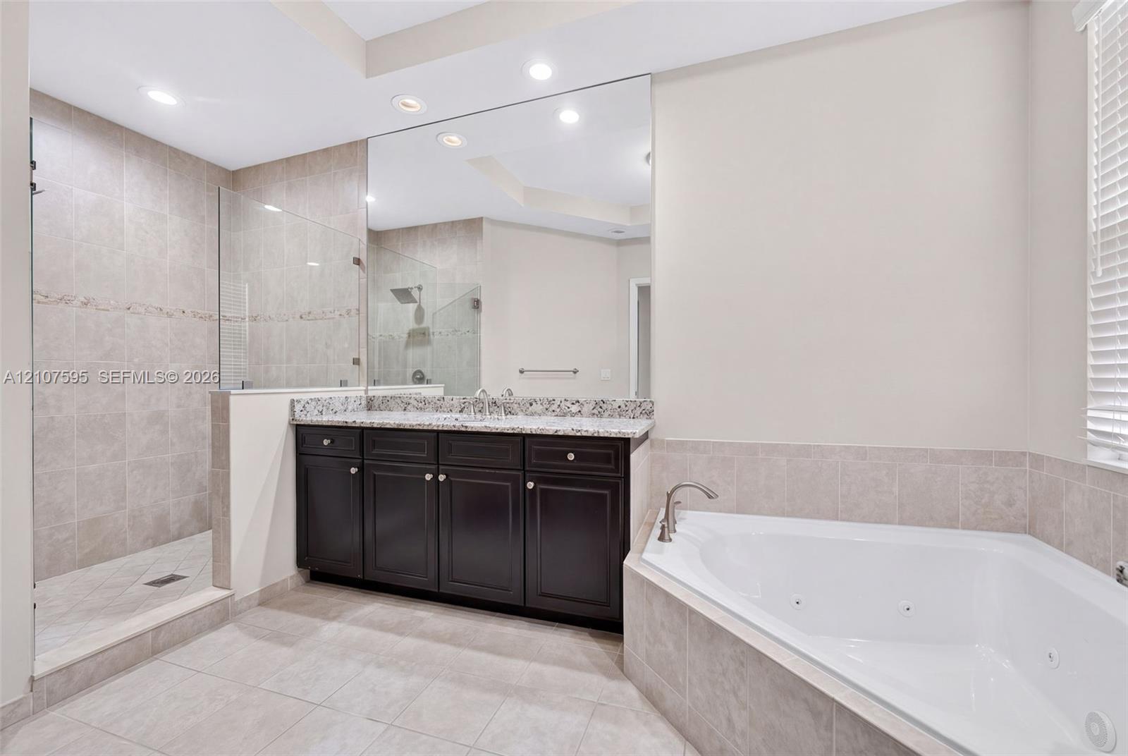 Bathroom featuring a dark wood vanity with a stone countertop, an oversized wall mirror, a corner jetted soaking tub, and a glass-enclosed walk-in shower with tile surrounds