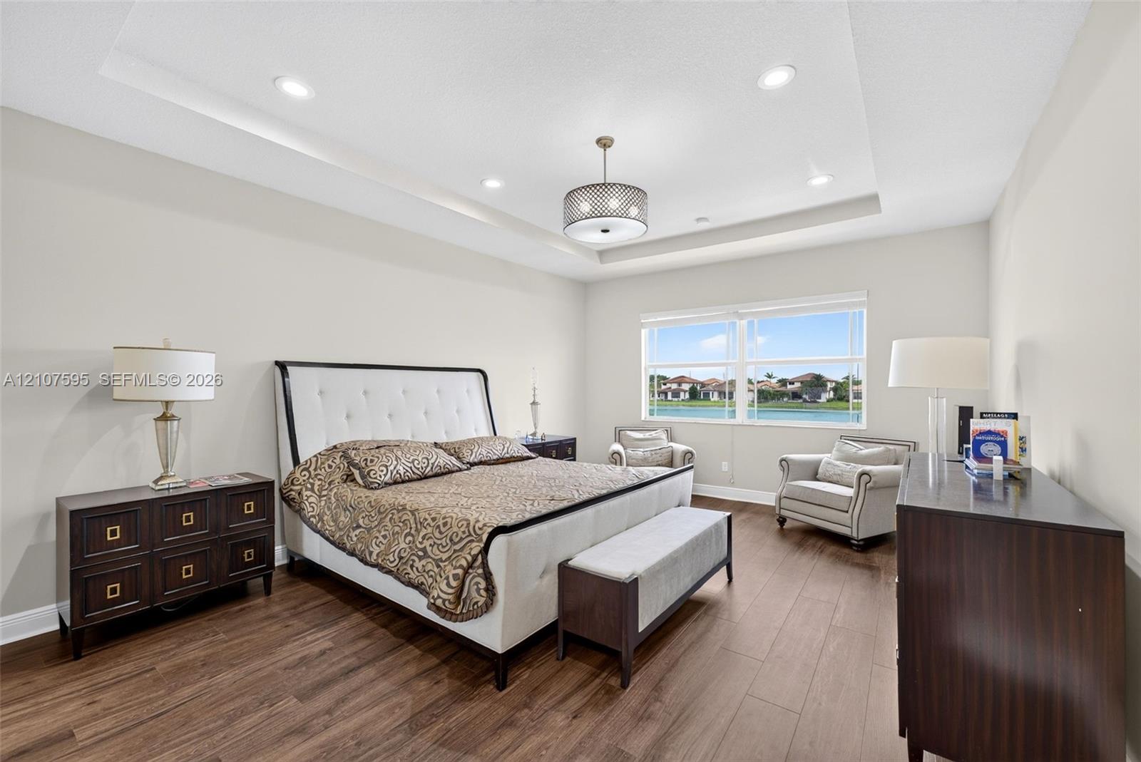 Tray ceiling with recessed lighting, central drum chandelier, and wood-finish flooring