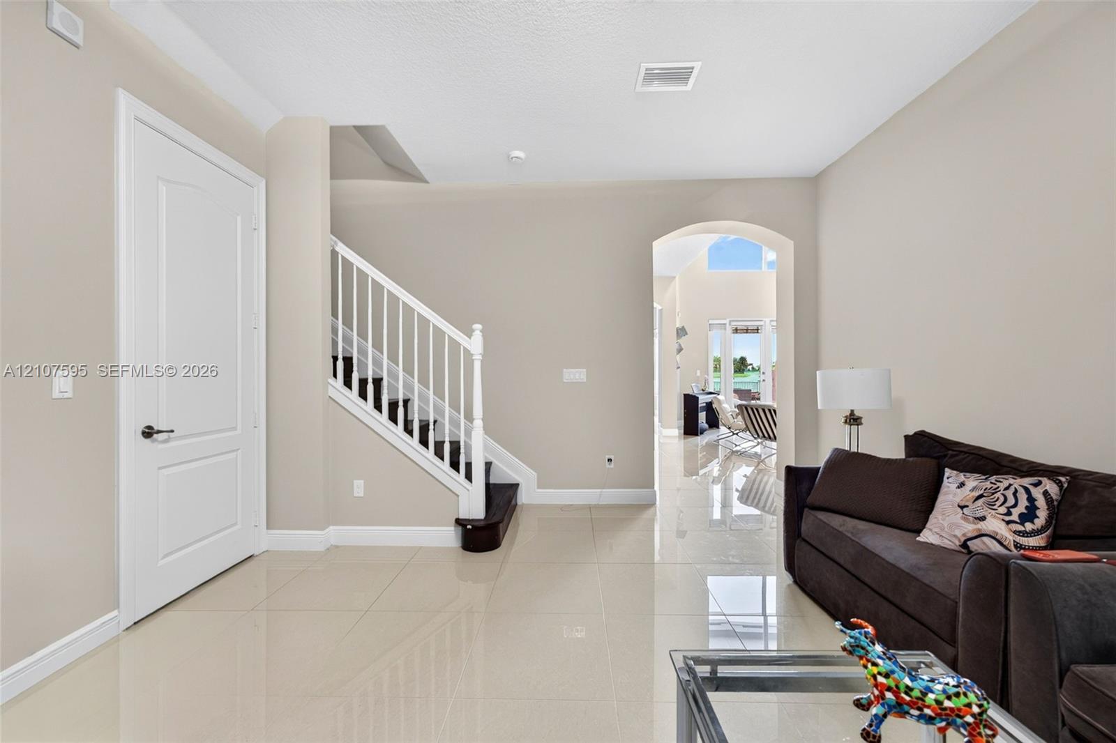 Polished tile flooring, staircase with white spindle railing, arched entryway, and neutral wall tones