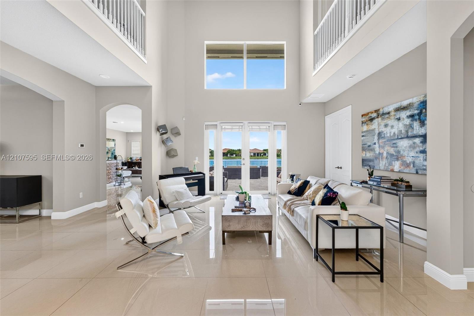 Grand foyer featuring soaring double-height ceilings, large-format tile flooring, a multi-story glass window configuration, arched architectural openings, and glass-paned double doors