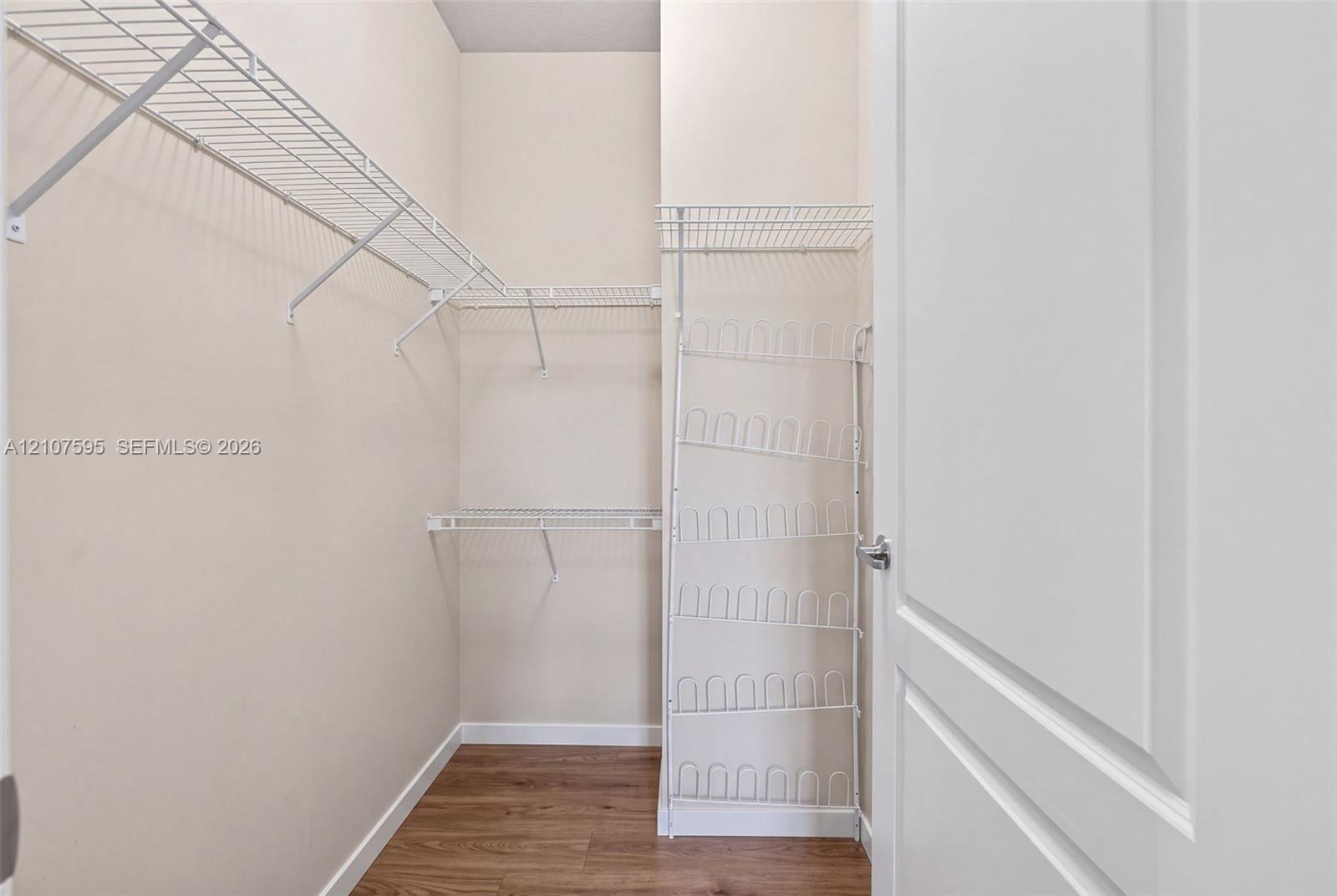 Walk-in storage space featuring wood-finish flooring, multi-level wire shelving, and an integrated vertical wire rack