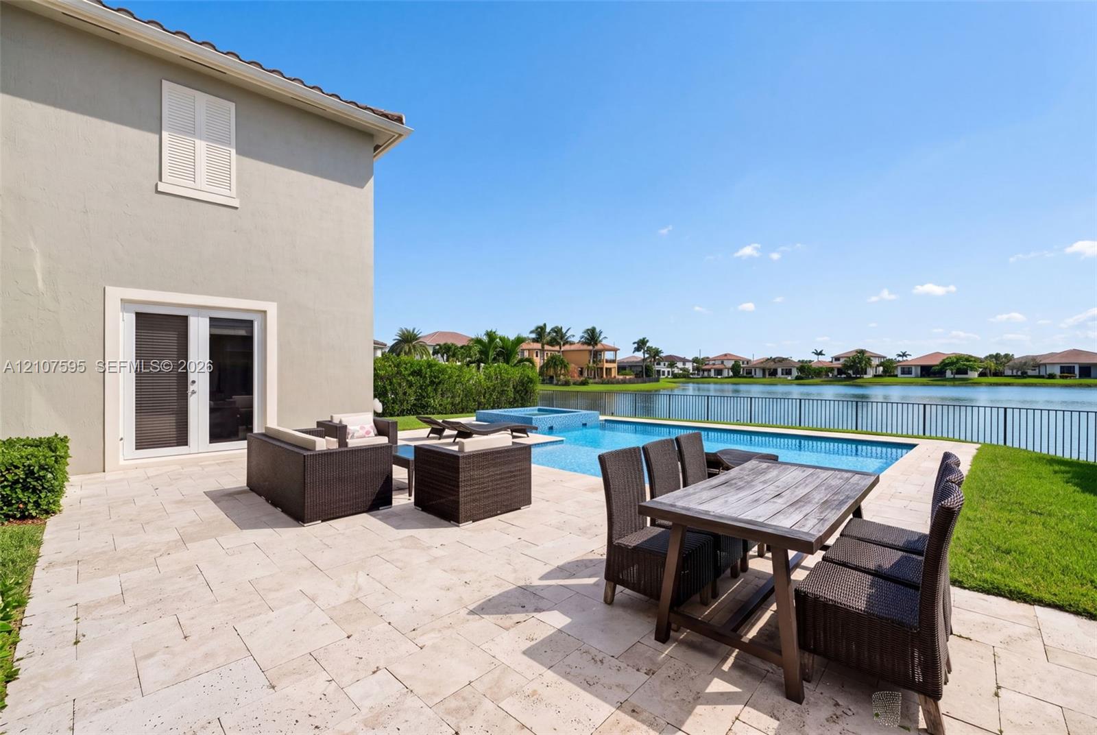 Rear exterior featuring a stone patio, in-ground swimming pool, attached spa, and metal perimeter fencing overlooking a lake