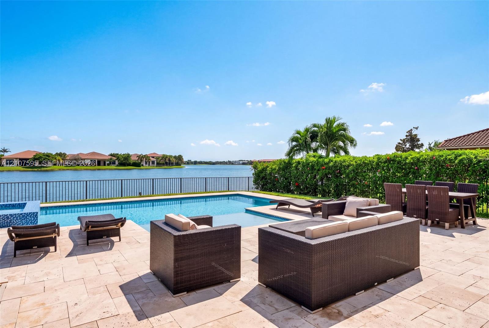 Stone-paved patio featuring a swimming pool, integrated spa, metal perimeter fencing, and mature hedge landscaping