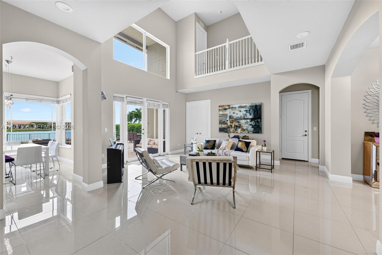 Double-height ceilings, large-format tile flooring, arched architectural detailing, sliding glass doors, and a decorative mezzanine railing