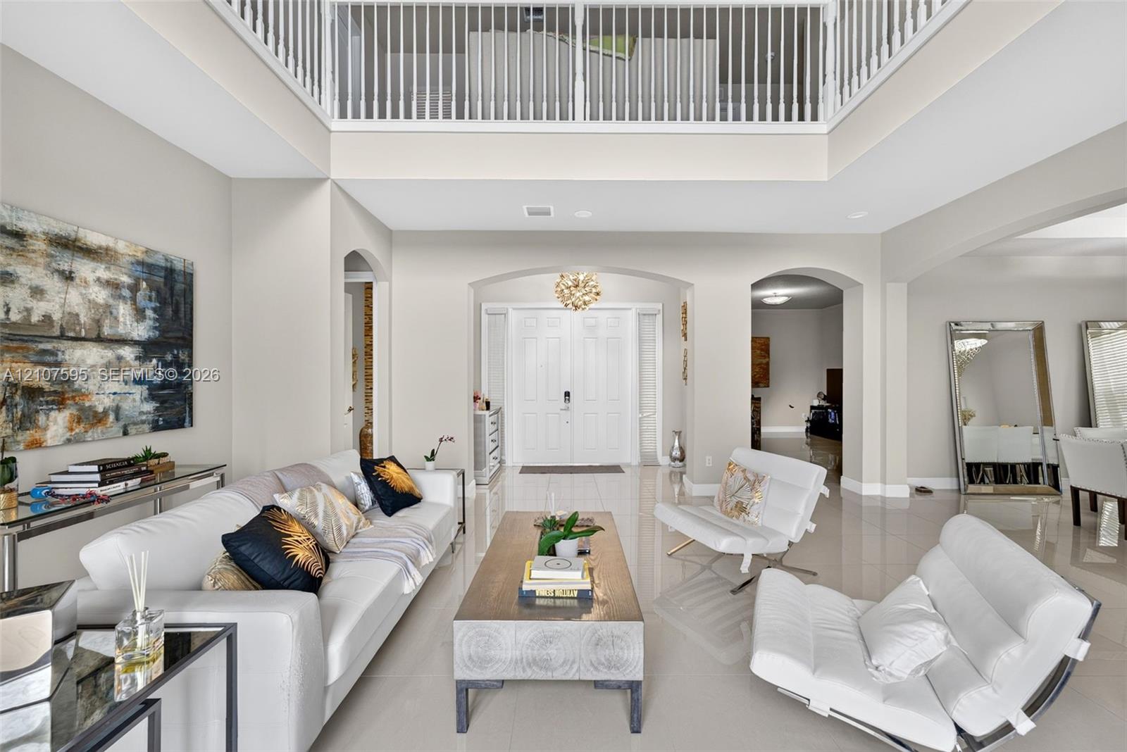 Double-height foyer featuring a mezzanine overlook, polished tile flooring, arched entryways, and double front doors