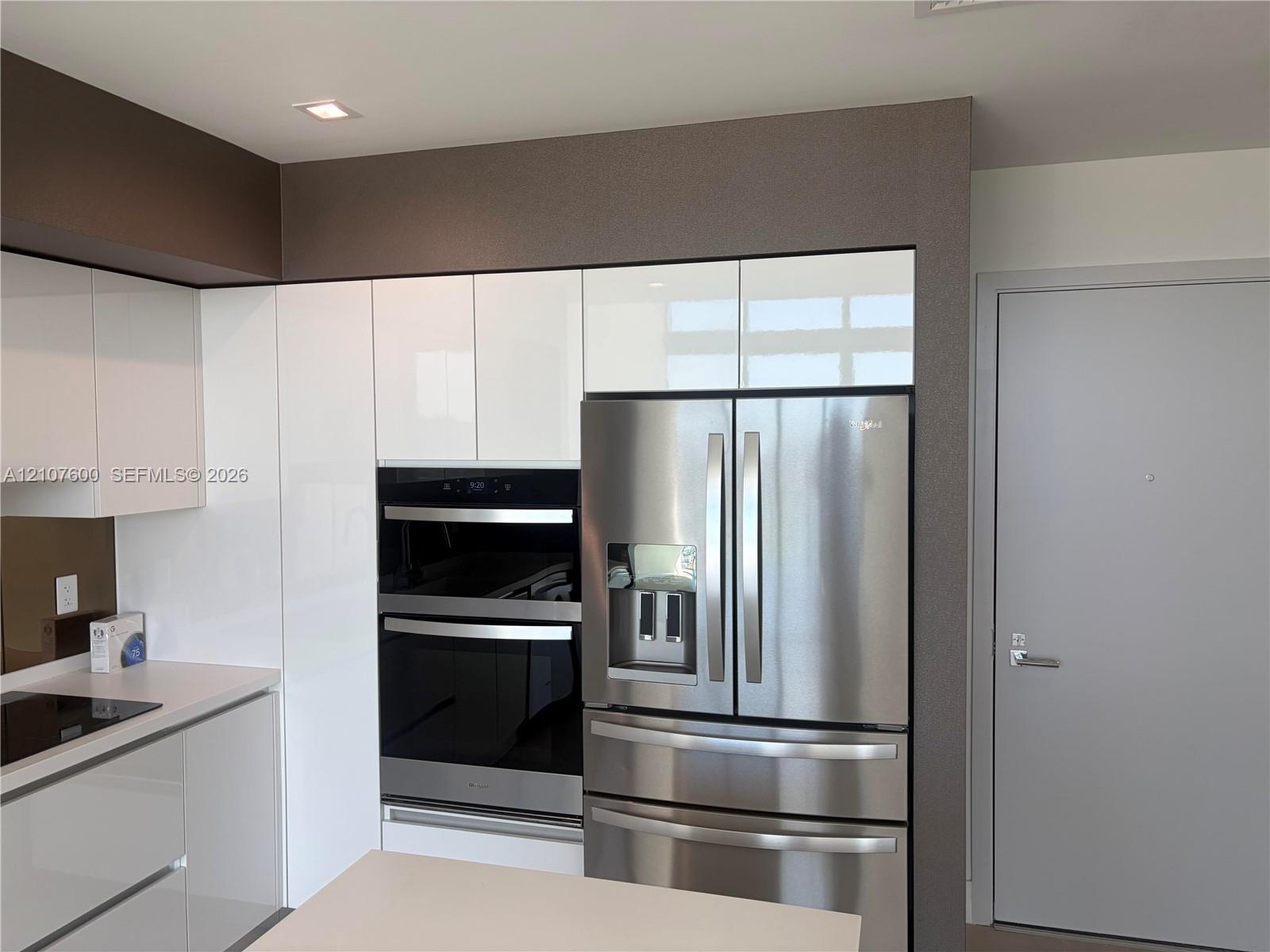 Glossy white cabinetry, built-in stainless steel double wall ovens, integrated stainless steel refrigerator, and recessed lighting Glossy white cabinetry, built-in stainless steel double wall ovens, integrated stainless steel refrigerator, and recessed lighting