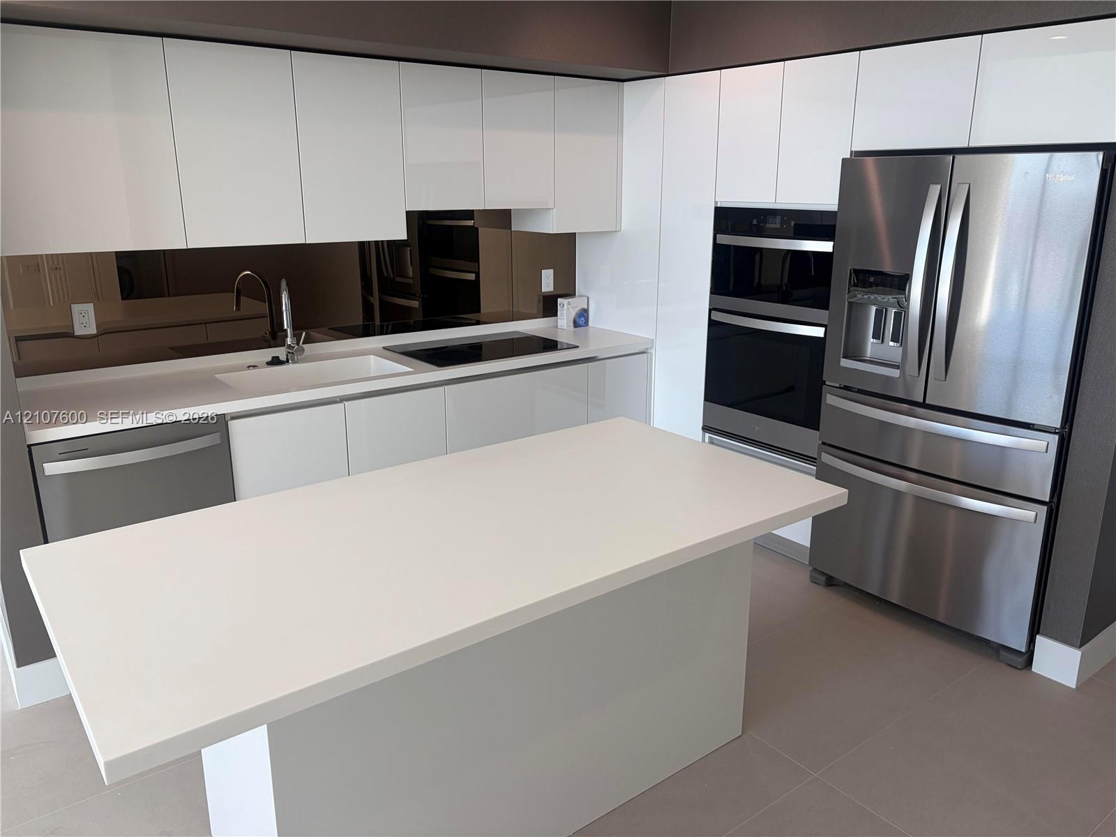 Kitchen featuring white high-gloss cabinetry, stone-surface countertops, a mirrored backsplash, stainless steel appliances, and a central island
