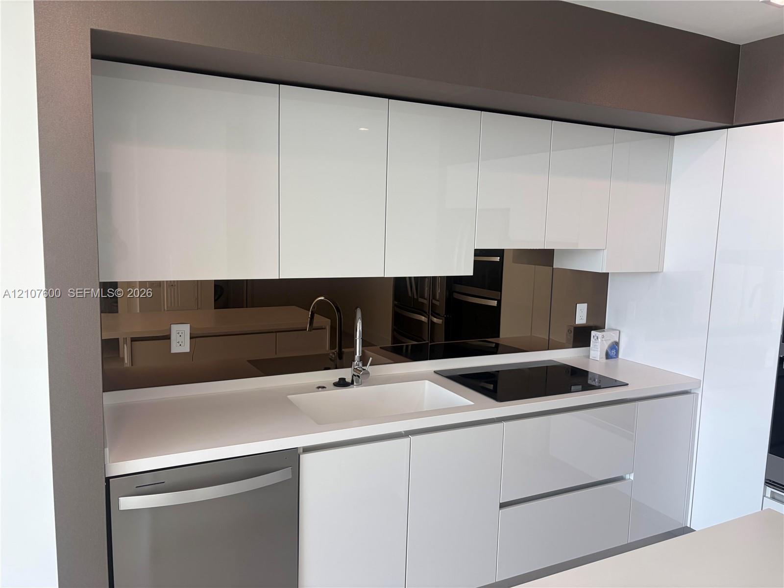 High-gloss cabinetry, integrated cooktop, undermount sink, solid surface countertop, and reflective backsplash High-gloss cabinetry, integrated cooktop, undermount sink, solid surface countertop, and reflective backsplash