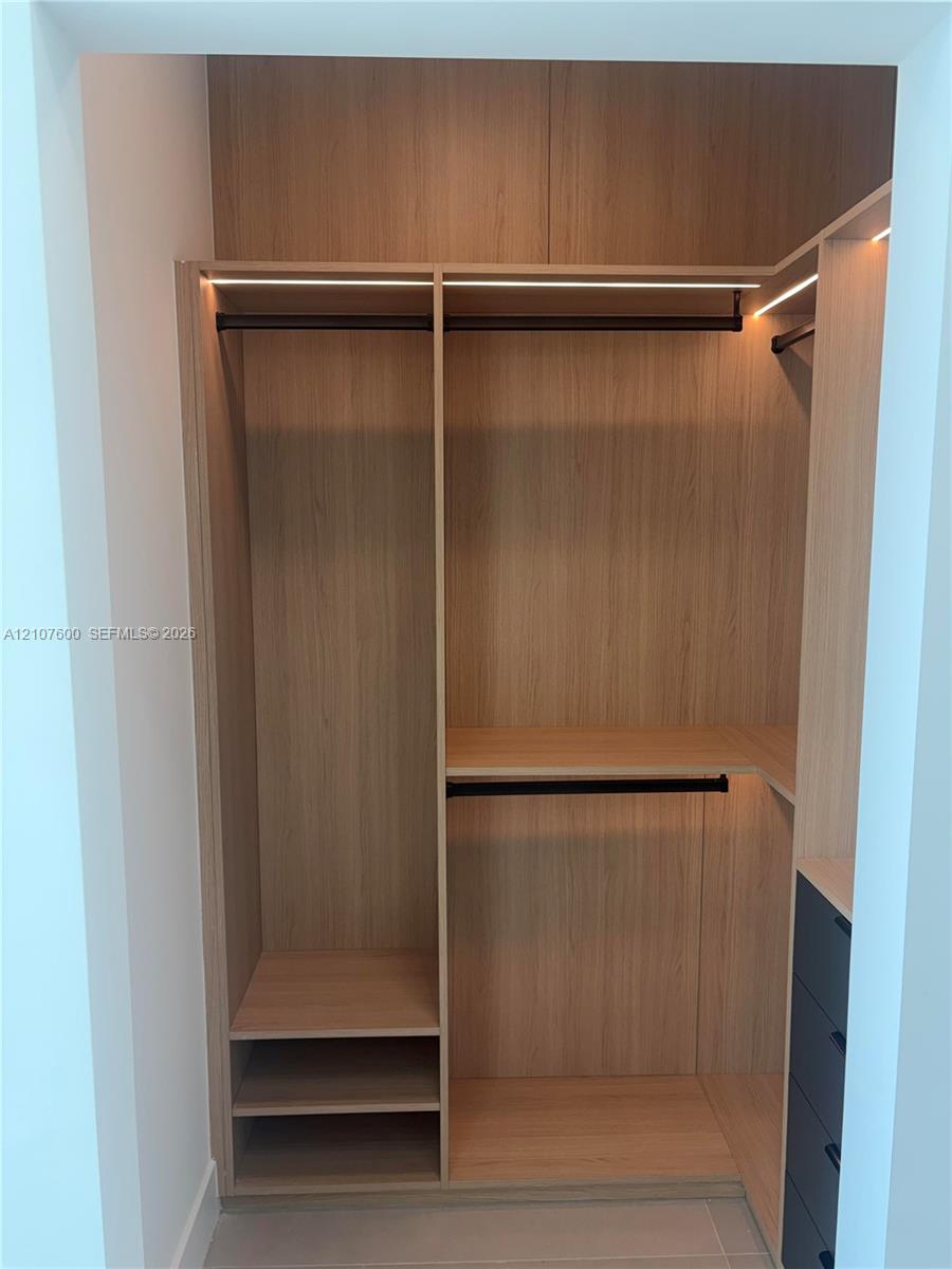 Custom storage cabinetry featuring wood-finish shelving, integrated linear lighting, matte black rods, and built-in drawer units