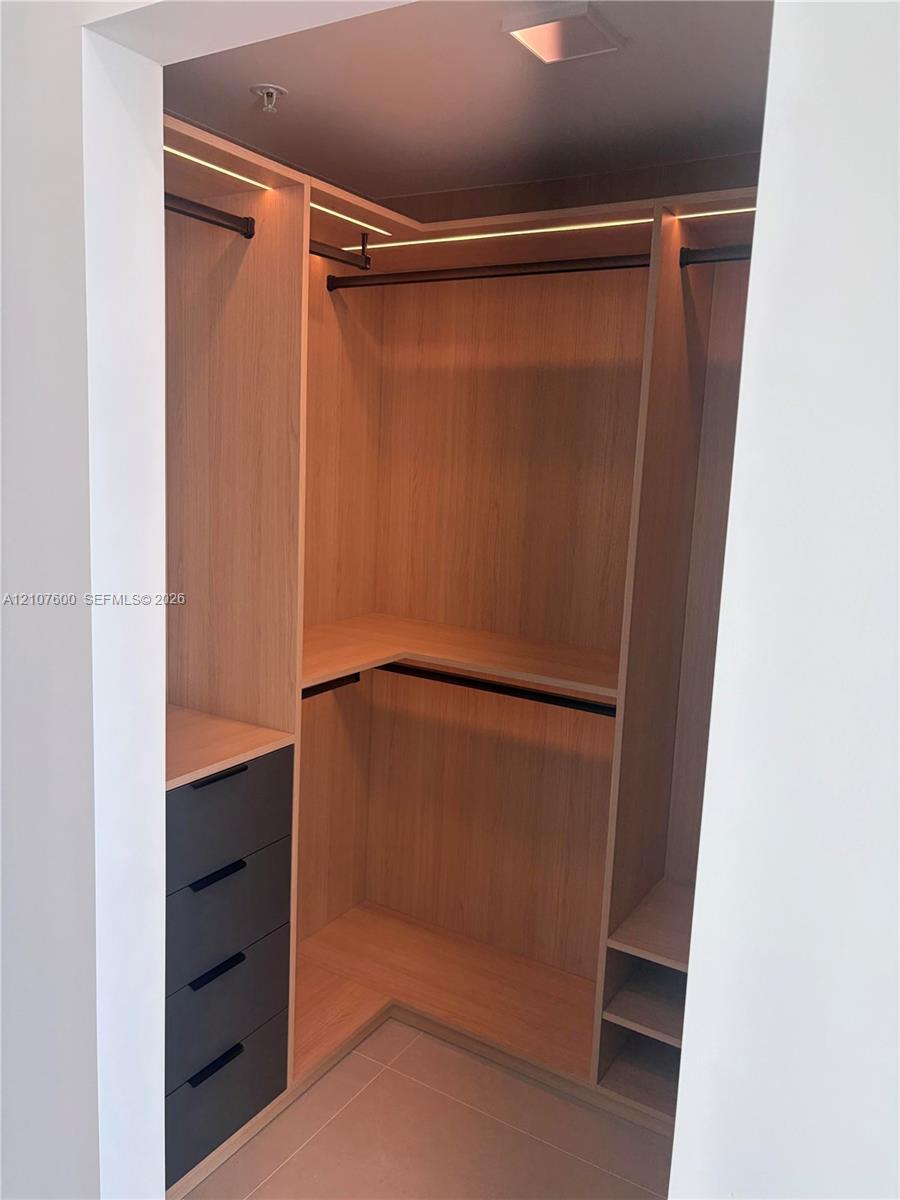 Custom reach-in closet featuring light wood-finish cabinetry, built-in drawer units with matte pulls, integrated LED strip lighting, and tiered shelving