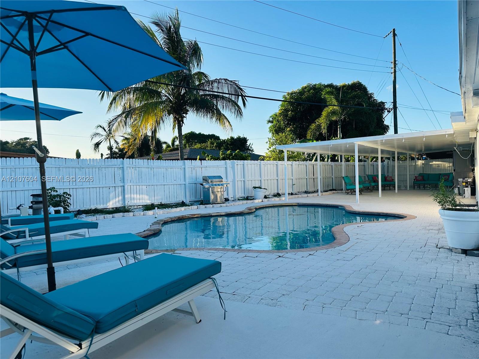Backyard featuring an in-ground swimming pool, stone paver decking, covered patio, and perimeter privacy fencing