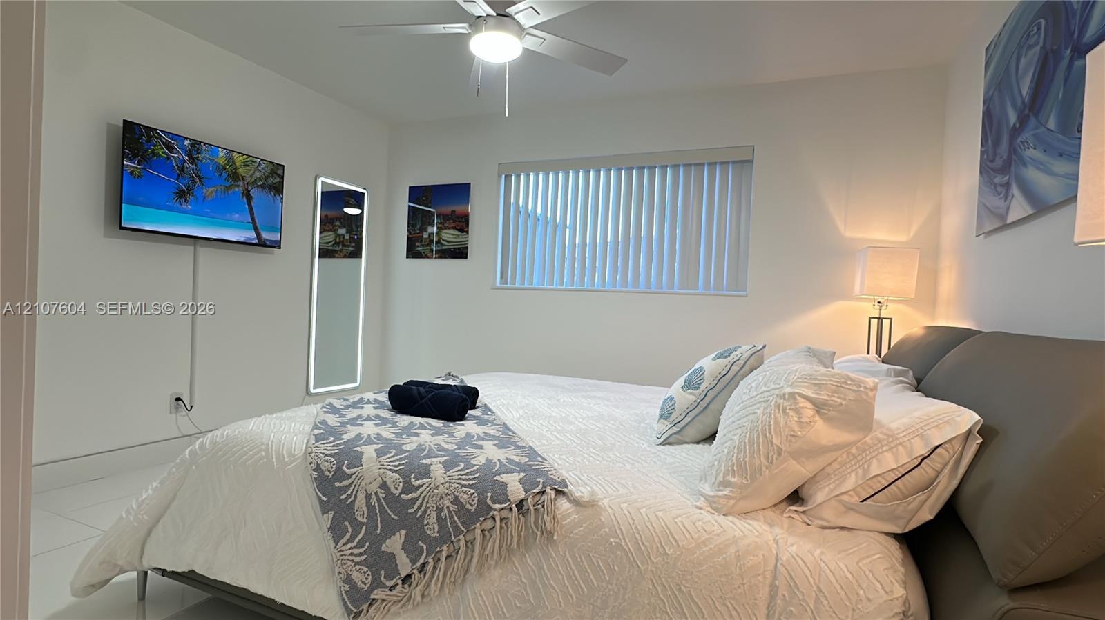 Neutral-toned interior featuring white tile flooring, a ceiling fan with integrated lighting, and vertical blinds