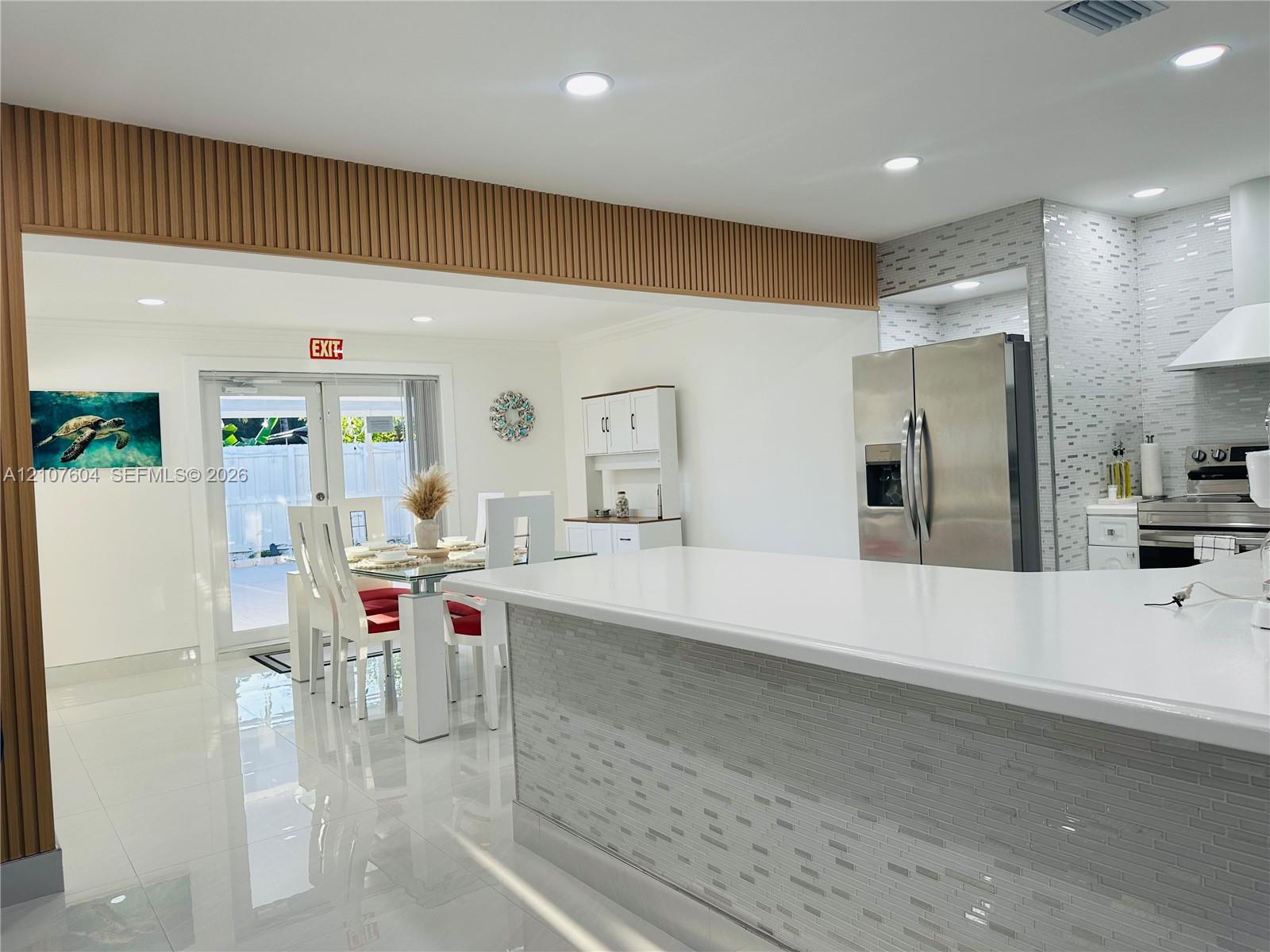Kitchen featuring a quartz countertop island, mosaic tile backsplash, stainless steel appliances, slat-style wood accent paneling, and polished tile flooring