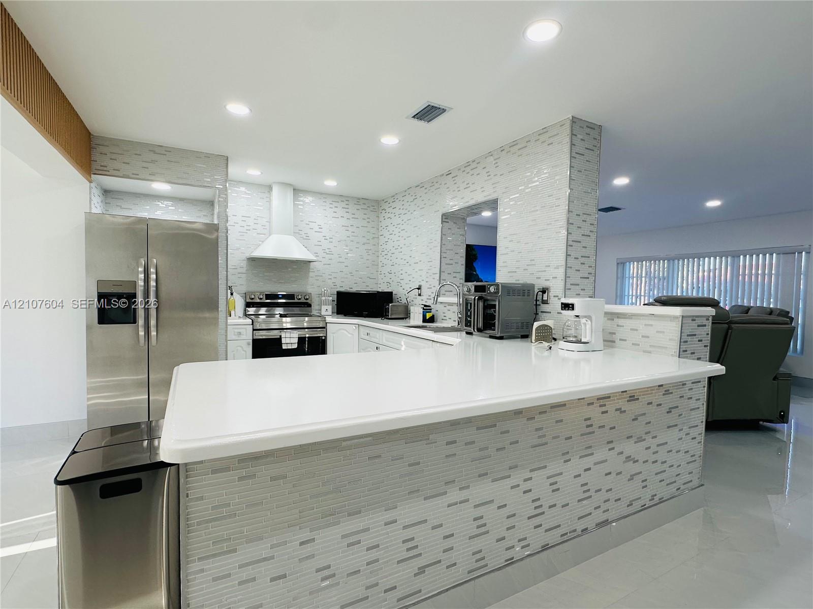 Kitchen featuring a solid surface countertop, stainless steel refrigerator, white range hood, and mosaic tile backsplash