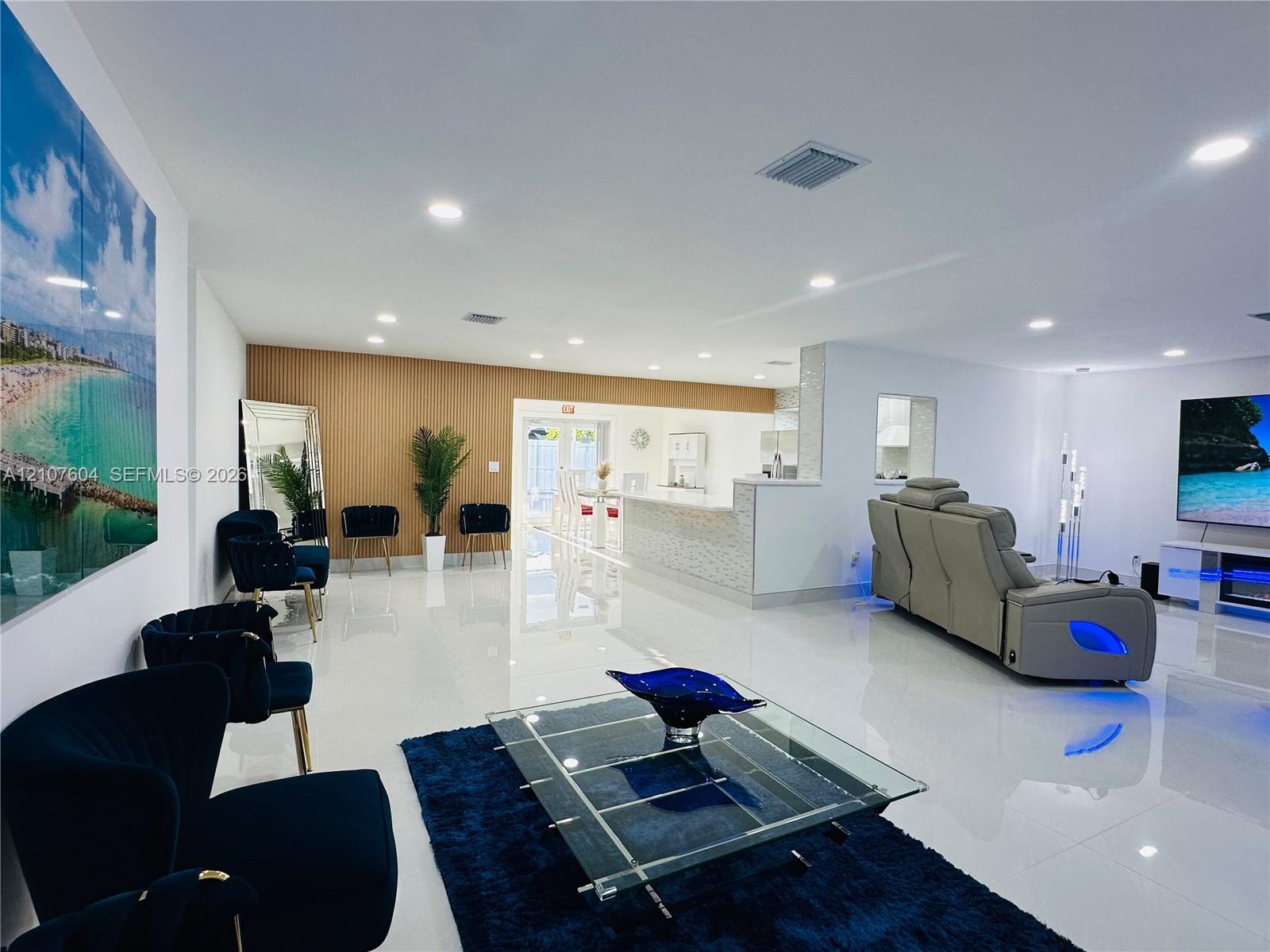 Open-concept interior featuring large-format polished flooring, wood-finish wall paneling, recessed lighting, and a kitchen island with stone-finish surfacing