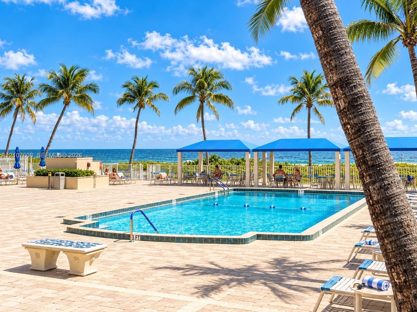 Swimming pool with tile edging, surrounding paver patio, and multiple blue-canopy cabanas situated near the coastline