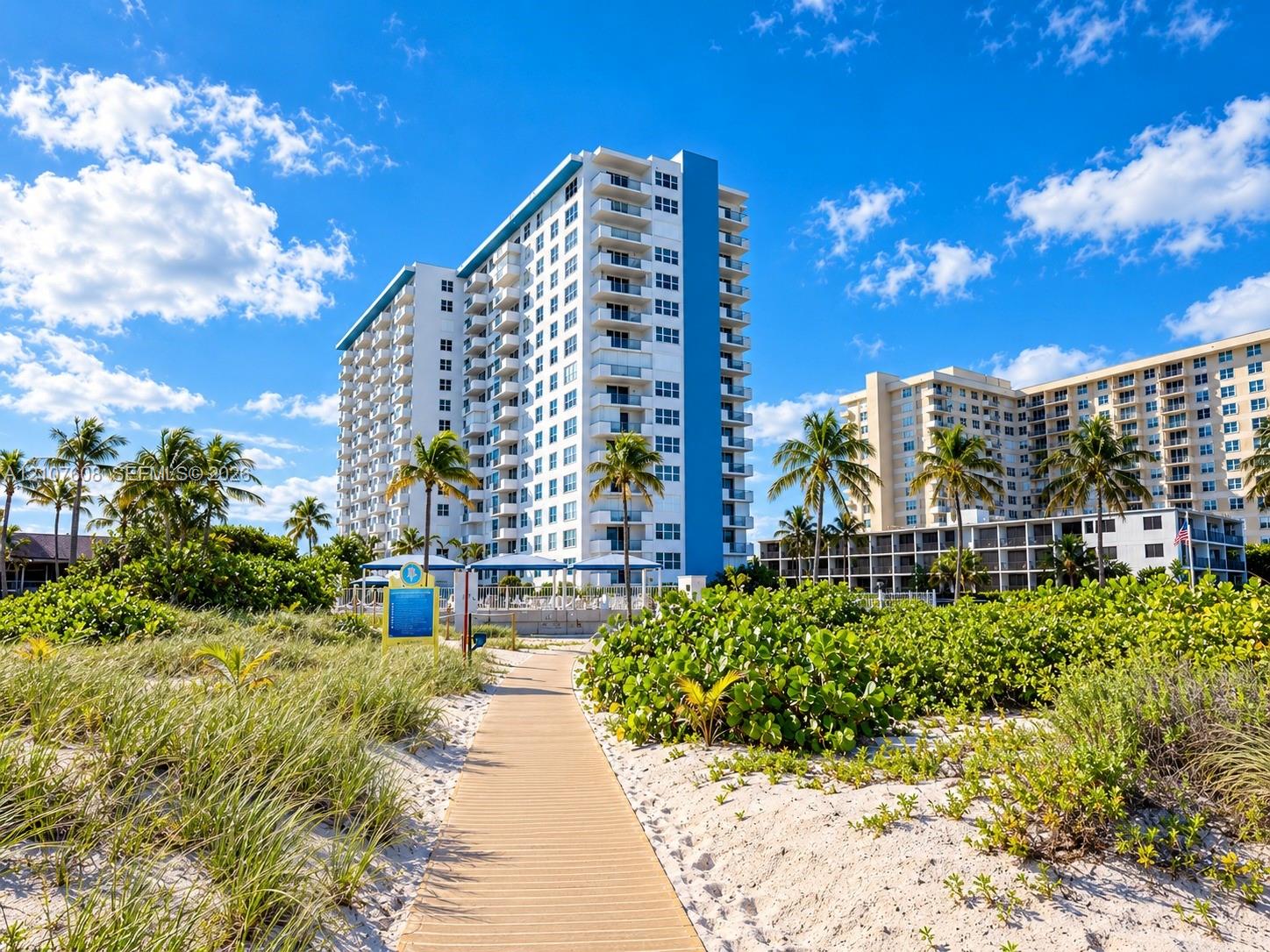 High-rise residential exterior featuring private balconies and a paved beach walkway surrounded by native coastal landscaping