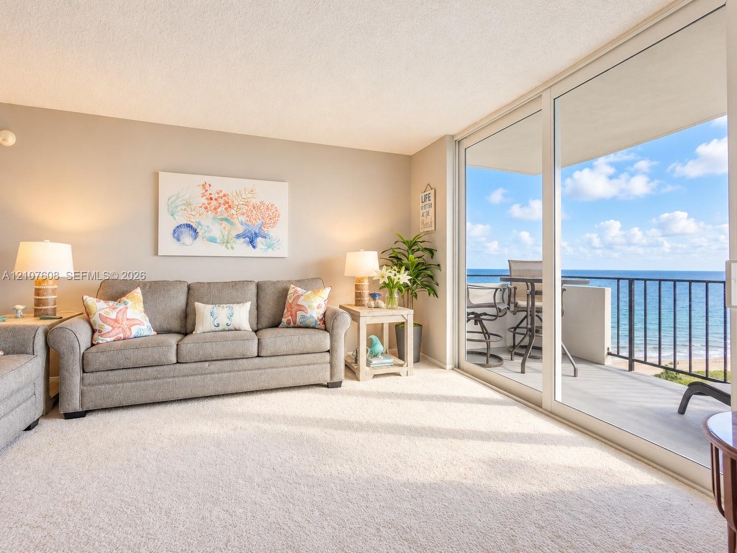 Living area featuring wall-to-wall carpeting and floor-to-ceiling sliding glass doors opening to a balcony with metal railings and coastal surroundings