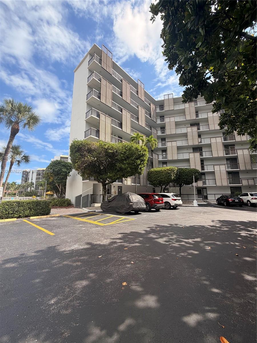 Mid-rise exterior featuring vertical architectural privacy screens, private balconies, and asphalt surface parking