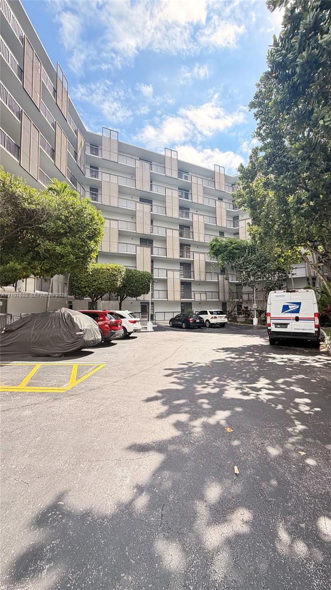 Mid-rise building exterior featuring a white facade, staggered balcony dividers, glass railings, and on-site surface parking