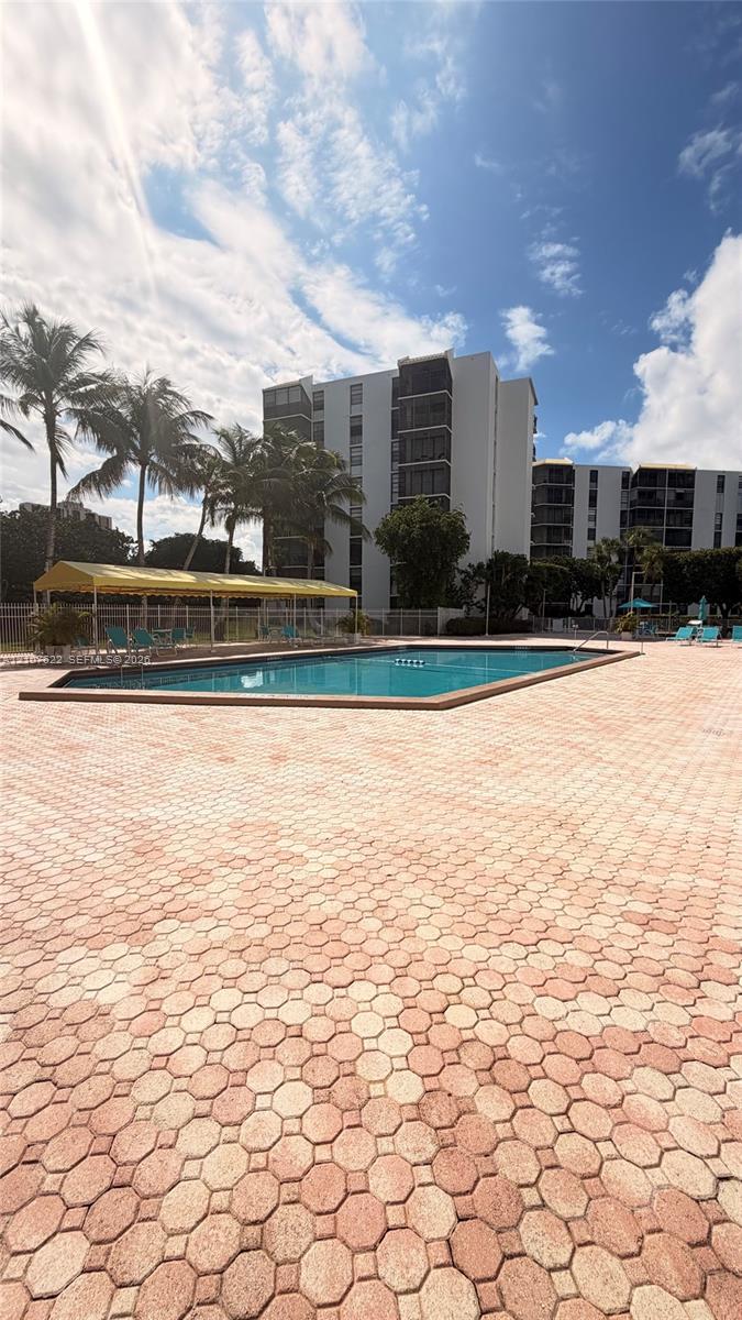 Outdoor pool featuring concrete paver decking and a covered shaded area