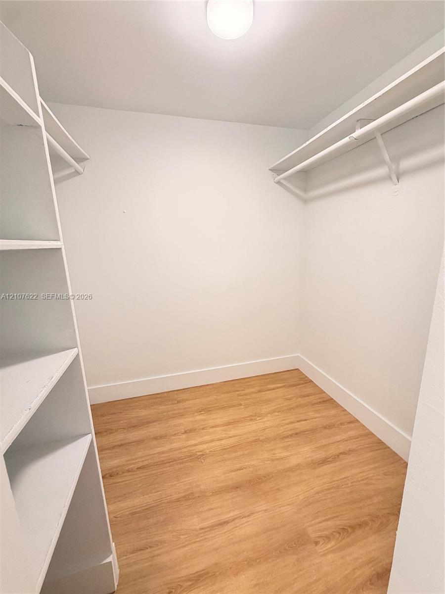 Walk-in closet featuring white built-in shelving, white overhead hanging rods, wood-finish flooring, and a central ceiling light fixture