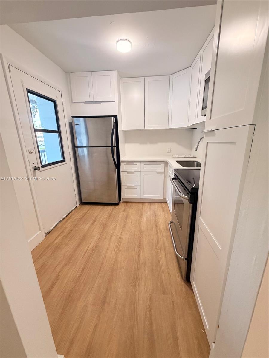 Kitchen featuring white shaker-style cabinetry, wood-finish flooring, stainless steel appliances, and solid surface countertops